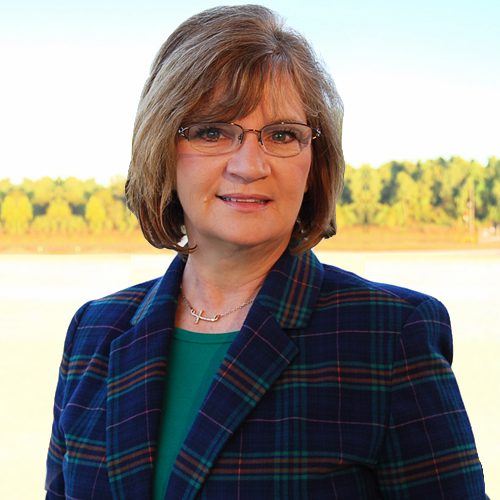 A portrait of a woman with glasses, wearing a plaid blazer, standing outdoors.