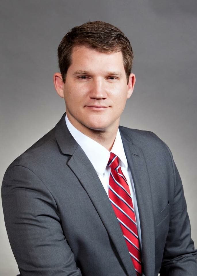 A man in a grey suit and red tie posing for a professional portrait.